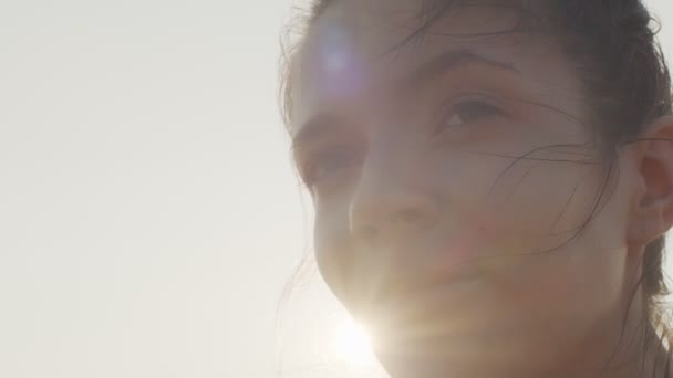 Hermosa cara femenina iluminada por el sol en el fondo del cielo blanco cerca de copiar el espacio de texto. Retrato al aire libre de mujer feliz mirando a lo lejos en el día de verano ventoso bengala lente de cámara lenta. Felicidad sueños libertad concepto — Vídeos de Stock