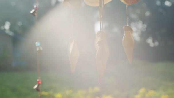 Marine wind chime made of seashells hanging outdoors backlit with sun rays lens flare. Tropical decoration spinning sunlit in summer sunlight slow motion. atmospheric wallpaper boho-chic style design — Stock Video