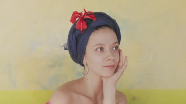 Porträt einer kaukasischen Frau mit blauem Turban und Blumen auf hellgelbem Hintergrund. Lächelndes natürliches Mädchen, das im tropischen Stil im Freien posiert, kopiert Text in Zeitlupe. Weibliche Hautpflege — Stockvideo