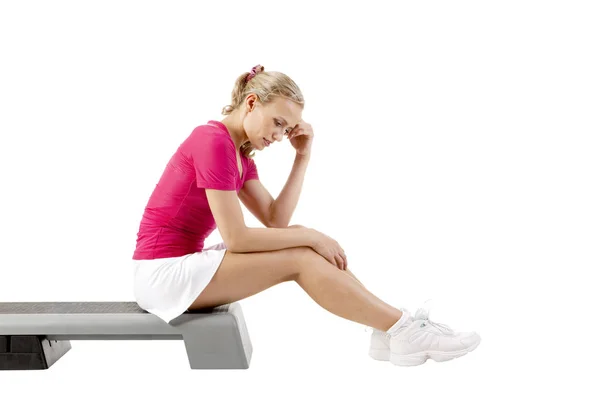 Ung kvinna trött efter sport sitter på fitness monter över vita b — Stockfoto