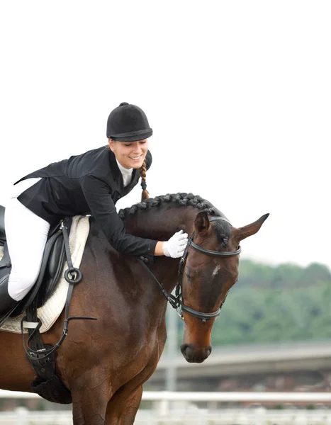 Attraktive junge Frau im Jockey-Anzug reitet und streichelt ihr Pferd — Stockfoto