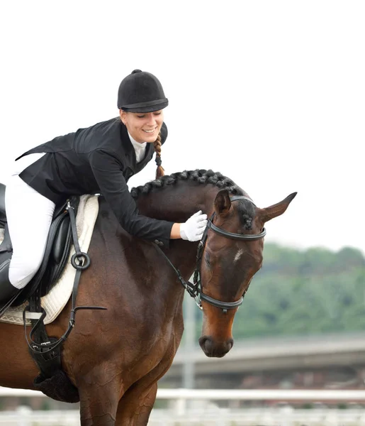 Attraktive junge Frau im Jockey-Anzug reitet und streichelt ihr Pferd — Stockfoto