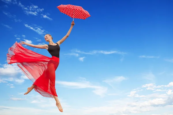 Молодая женщина прыгает в небо с красным зонтиком — стоковое фото