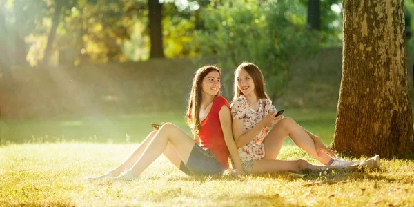 Chicas felices sentadas con teléfonos móviles en el prado de verano —  Fotos de Stock
