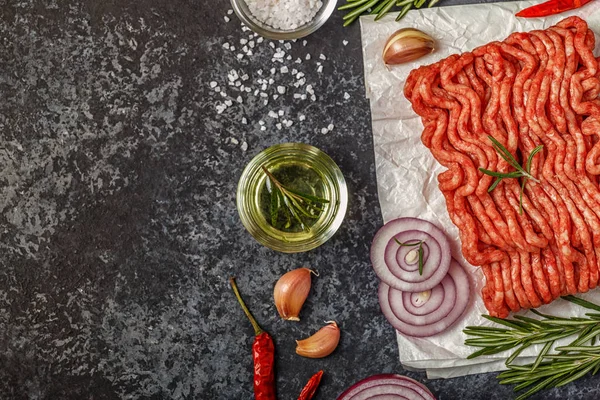 Raw minced meat on paper with onion, herbs and seasonings on bla