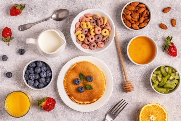 Breakfast with colorful cereal rings, pancakes, fruit, milk, jui
