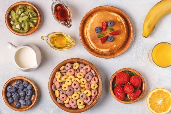 Breakfast with colorful cereal rings, pancakes, fruit, milk, jui