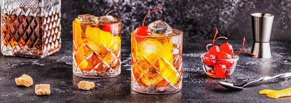 Old fashioned cocktail with cherries and orange twist.