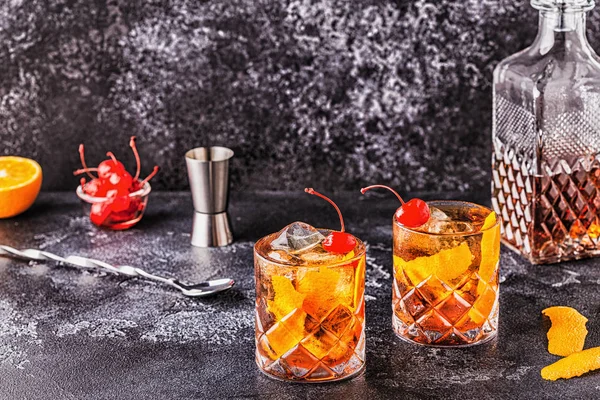 Old fashioned cocktail with cherries and orange twist.