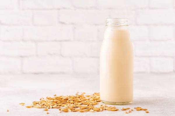 A bottle of oat milk and oats on a light background.