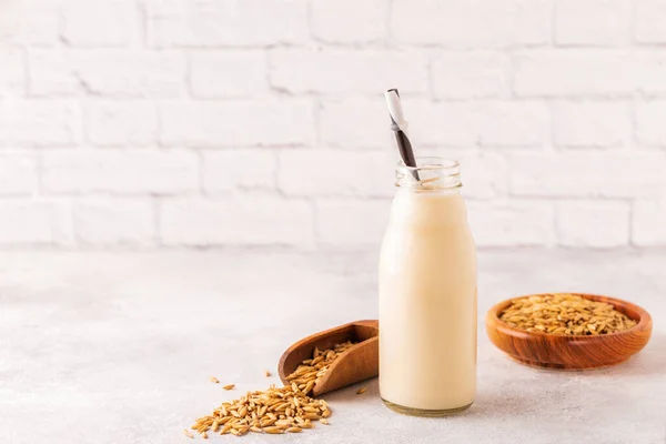 A bottle of oat milk and oats on a light background.