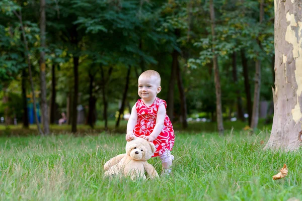 Une fille joue avec un ours en peluche dans un parc sur une herbe — Photo