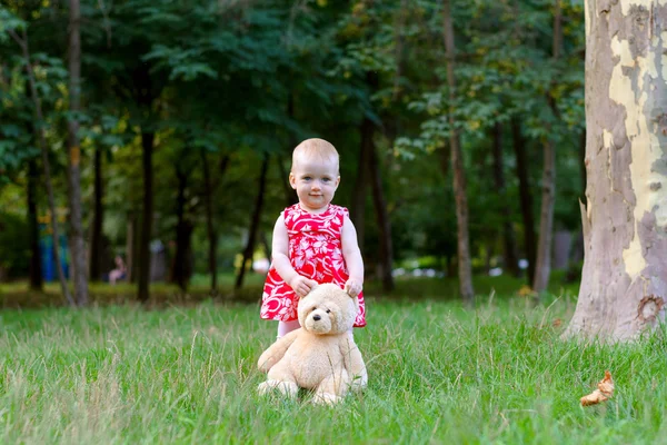 Une fille joue avec un ours en peluche dans un parc sur une herbe — Photo