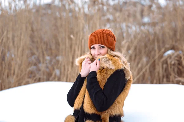 Vacker flicka i en päls väst promenader i ett fält i snön — Stockfoto