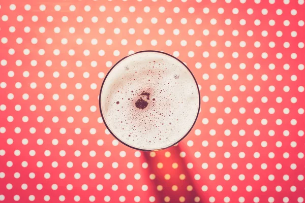 Overhead shot of beer glass on red dotted background