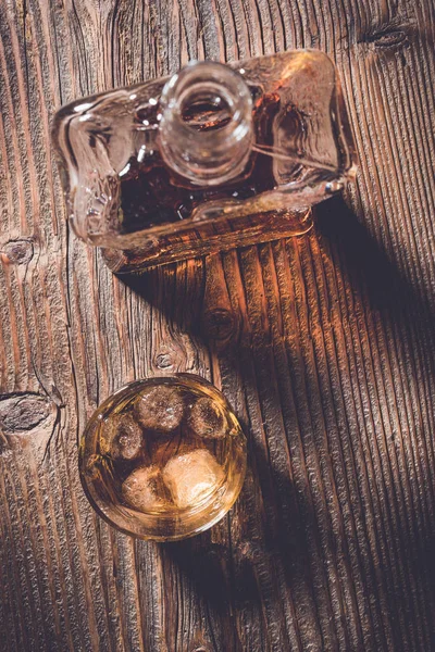 Bardak viski buz küpleri ve viski şişesi üzerinde eski bir ahşap masa