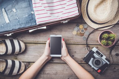 Seyahat hazırlıkları konseptiyle bavul, giysi ve aksesuarları eski ahşap masa. Üstten Görünüm