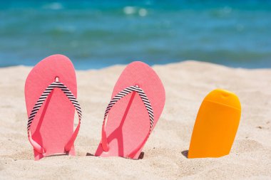 Güneş kremi şişe ve sahilde pembe flip flop