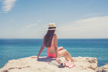 Genç kadın uzun saçlı cliff üzerinde oturan ve denizde seyir