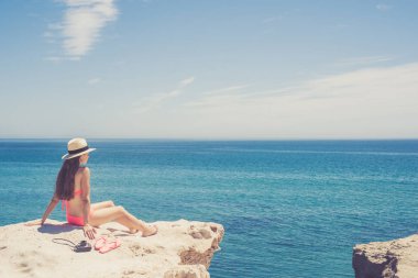 Genç kadın uzun saçlı cliff üzerinde oturan ve denizde seyir