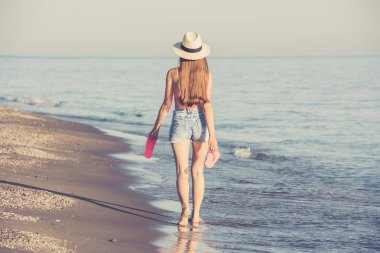 Genç bir kadın sahilde yürüyor.