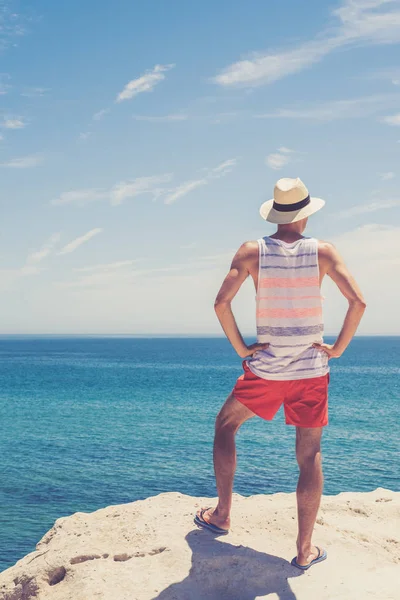 Retrato de jovem atraente homem de pé no penhasco e olhando para o oceano — Fotografia de Stock