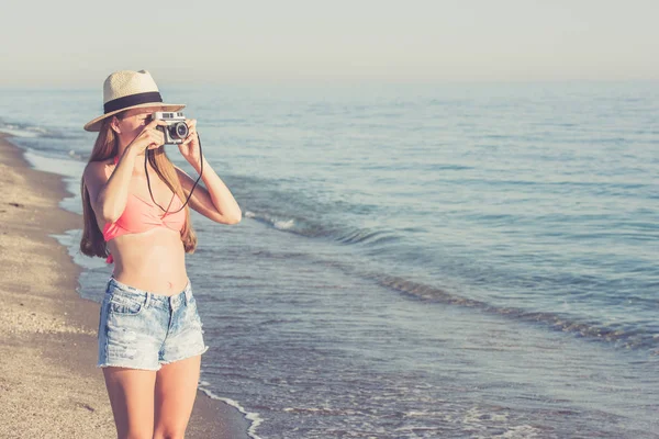 Jovem mulher tirando foto na praia usando câmera retro — Fotografia de Stock