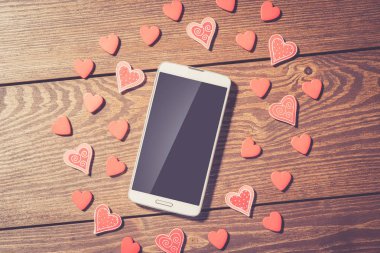 Kırmızı Kalpler ve eski bir ahşap masa boş ekran ile beyaz akıllı telefon