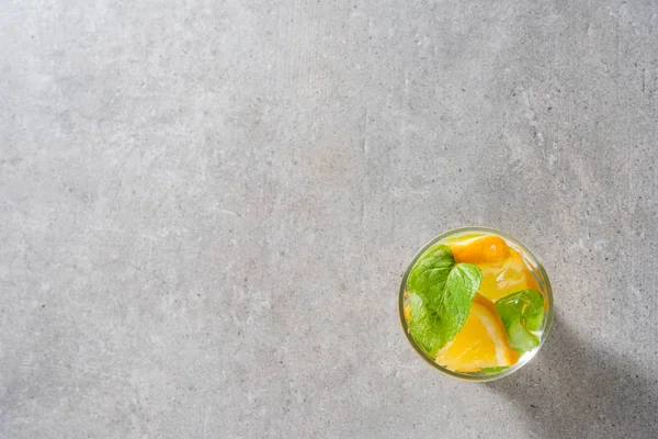 Refreshing orange drink with mint leaves and ice on gray stone table
