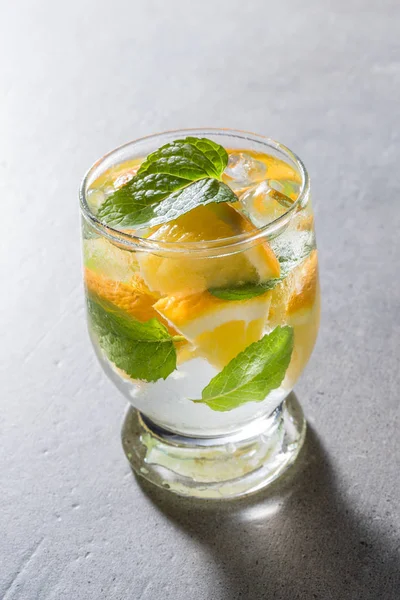 Refreshing orange drink with mint leaves and ice on gray stone table
