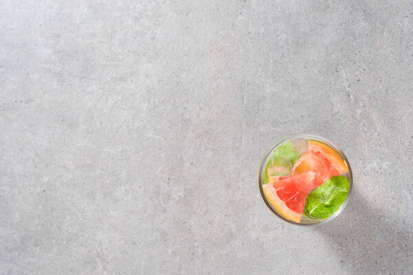 Refreshing grapefruit drink with mint leaves and ice on gray stone table