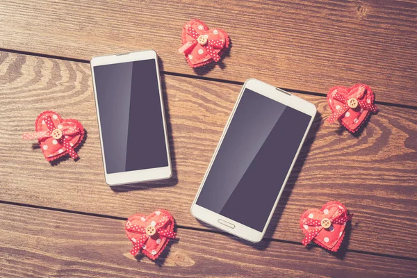 Red hearts and white smart phone with blank screen on an old wooden table
