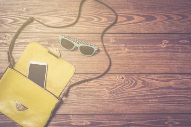 Beyaz akıllı telefon ve ahşap masa üzerinde güneş gözlüğü ile kadın çanta