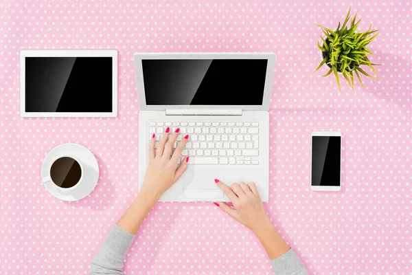 Mujer usando el ordenador portátil moderno sobre la mesa de puntos rosa — Foto de Stock