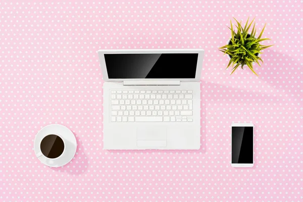 Pink office desktop with white laptop, smart phone and coffee cup.