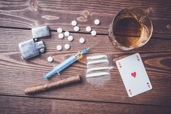 Drogas duras con pastillas, naipes, jeringa y alcohol en la mesa de madera — Foto de Stock