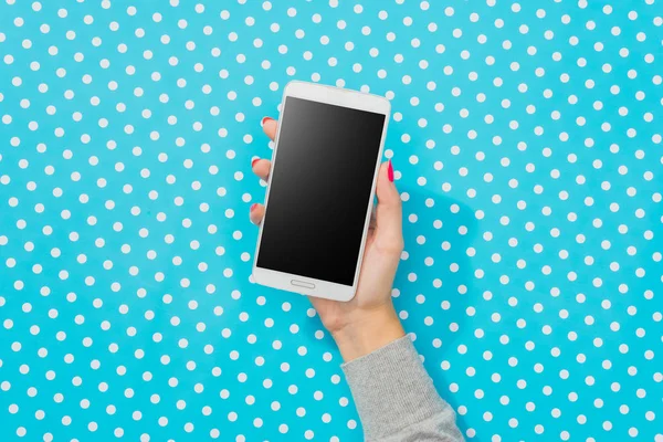 Manos femeninas usando teléfono inteligente blanco sobre fondo punteado azul — Foto de Stock