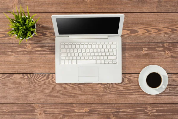 Vista aérea de la mesa de oficina con portátil blanco, taza de café y planta verde — Foto de Stock