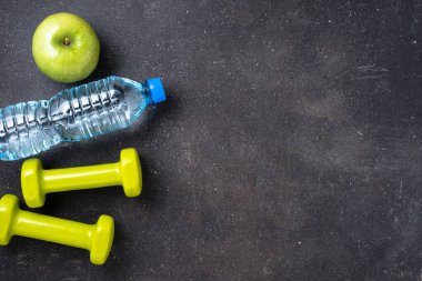 Fitness kavramı dambıl, su ve koyu arka plan üzerinde yeşil elma