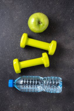 Fitness kavramı dambıl, su ve koyu arka plan üzerinde yeşil elma