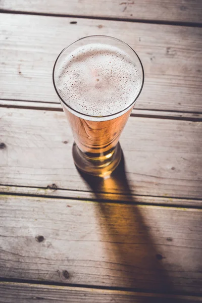 Un vaso de cerveza en una vieja mesa de madera . — Foto de Stock