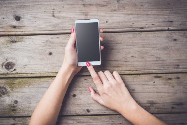 Ahşap masa üzerinde beyaz akıllı telefon kullanan kadın