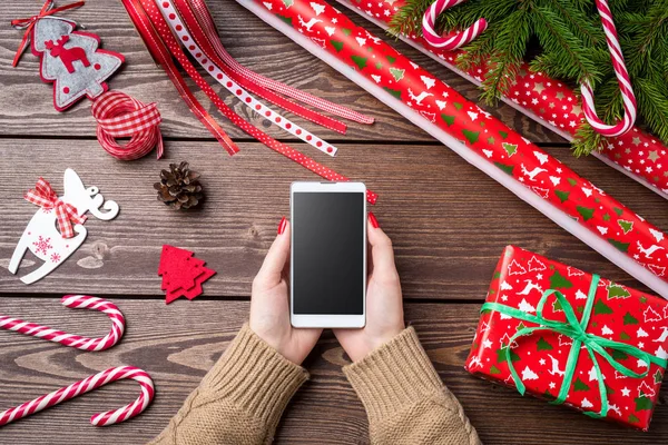 Mulher segurando telefone inteligente sobre mesa de madeira. Conceito de preparações de Natal . — Fotografia de Stock