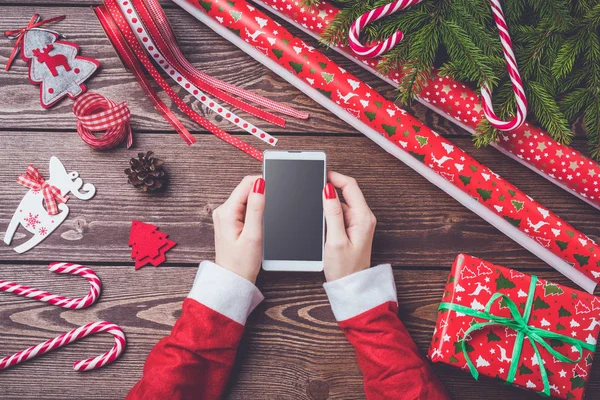 Mulher segurando telefone inteligente sobre mesa de madeira. Conceito de preparações de Natal . — Fotografia de Stock