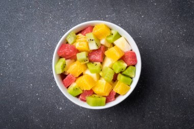 Renkli meyve salatası gri taş masada.