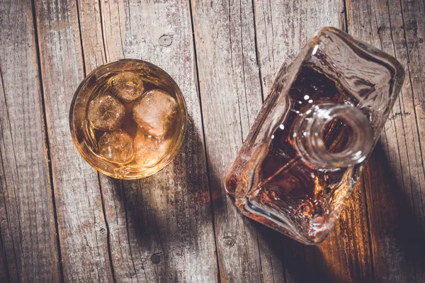 Overhead shot of whiskey bottle and whiskey glass with ice cubes on an old wooden table