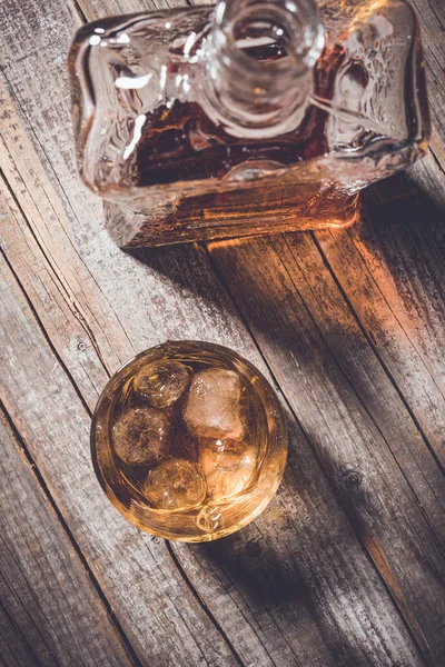 Fotografia aérea de garrafa de uísque e copo de uísque com cubos de gelo em uma velha mesa de madeira — Fotografia de Stock