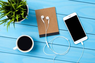 Beyaz akıllı telefon ve aksesuarları mavi ahşap masa üzerinde. Üstten görünüm