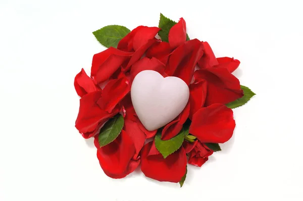 White ceramic heart lying on the bed of rose petals and leaves o — Stock Photo, Image