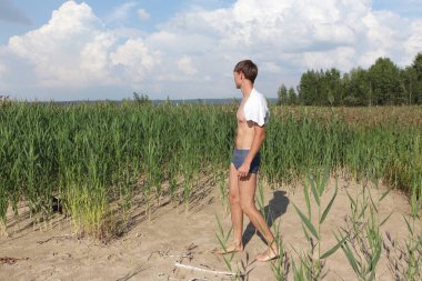 Nehir kıyısındaki omuzlarında bir havlu ile giden genç adam  